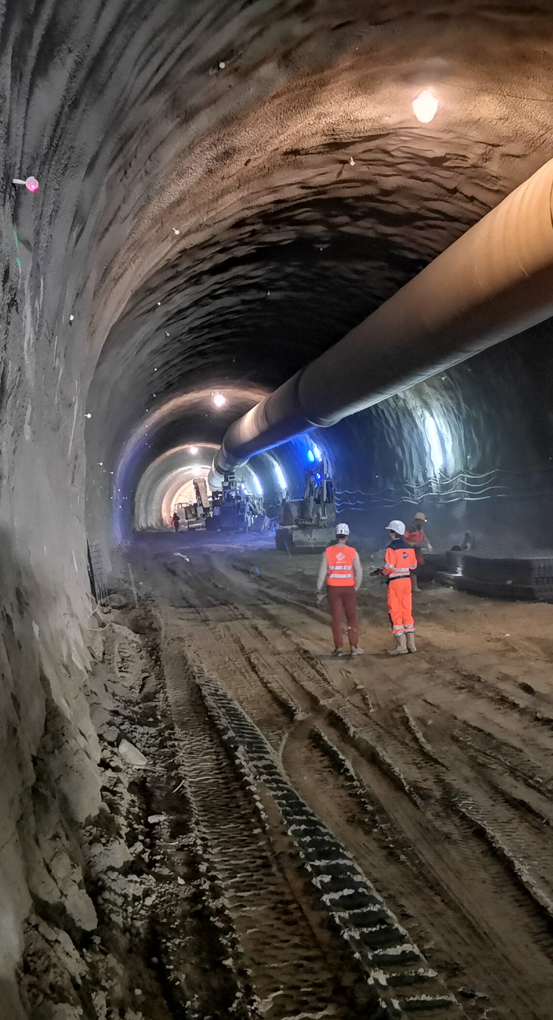 Tunnel im Bauzustand mit Belüftungsrohr und zwei Personen mit Helm und Schutzbekleidung